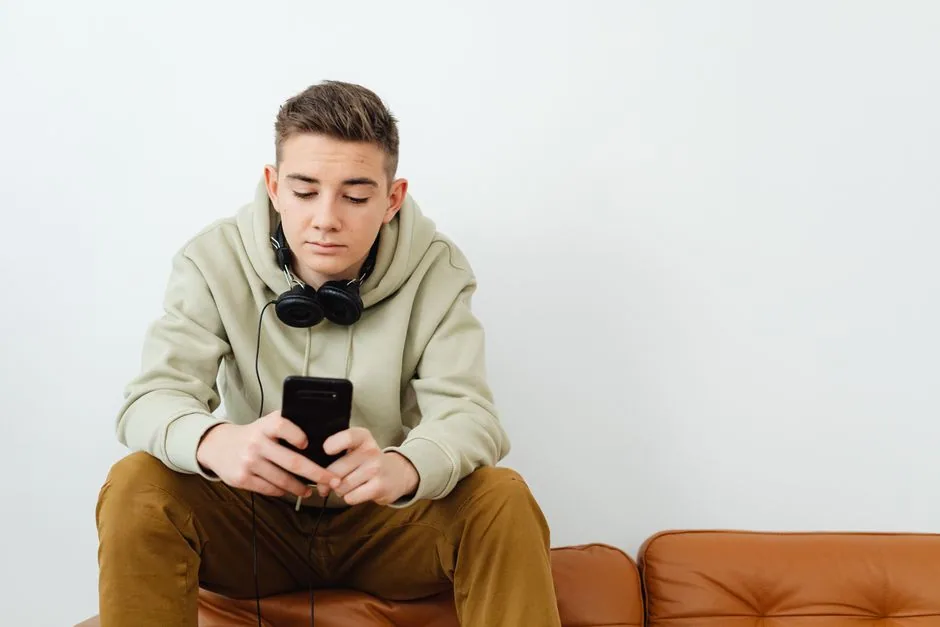 Jugendlicher liegt mit Kopfhörern und Smartphone auf dem Sofa