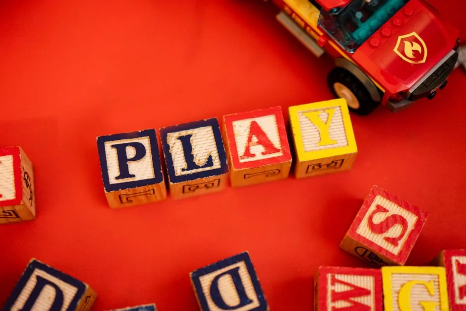Holzbausteine, die das Wort PLAY bilden, daneben ein Spielzeugauto
