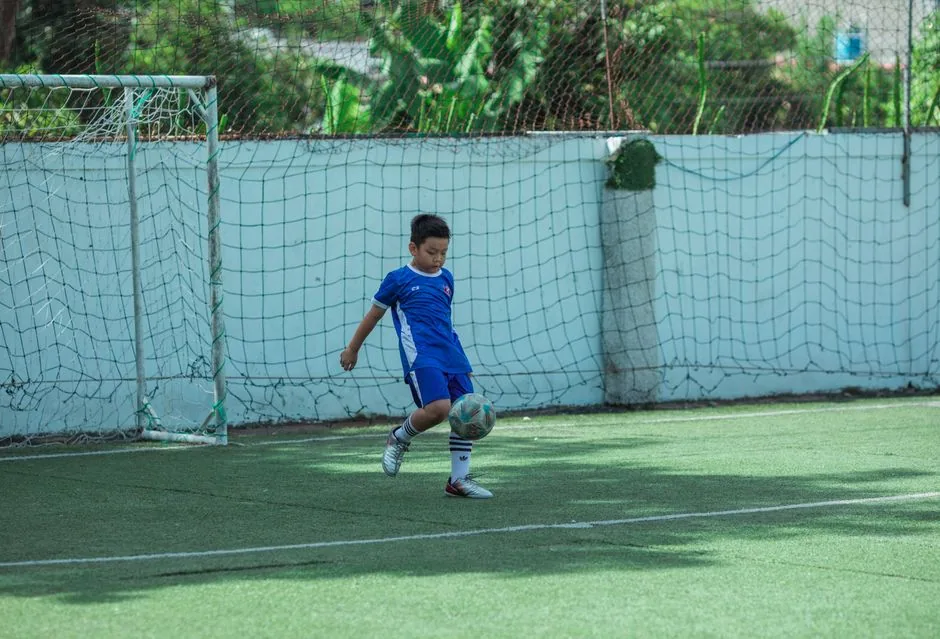 Junge im blauen Trikot spielt auf einem Rasenplatz Fußball