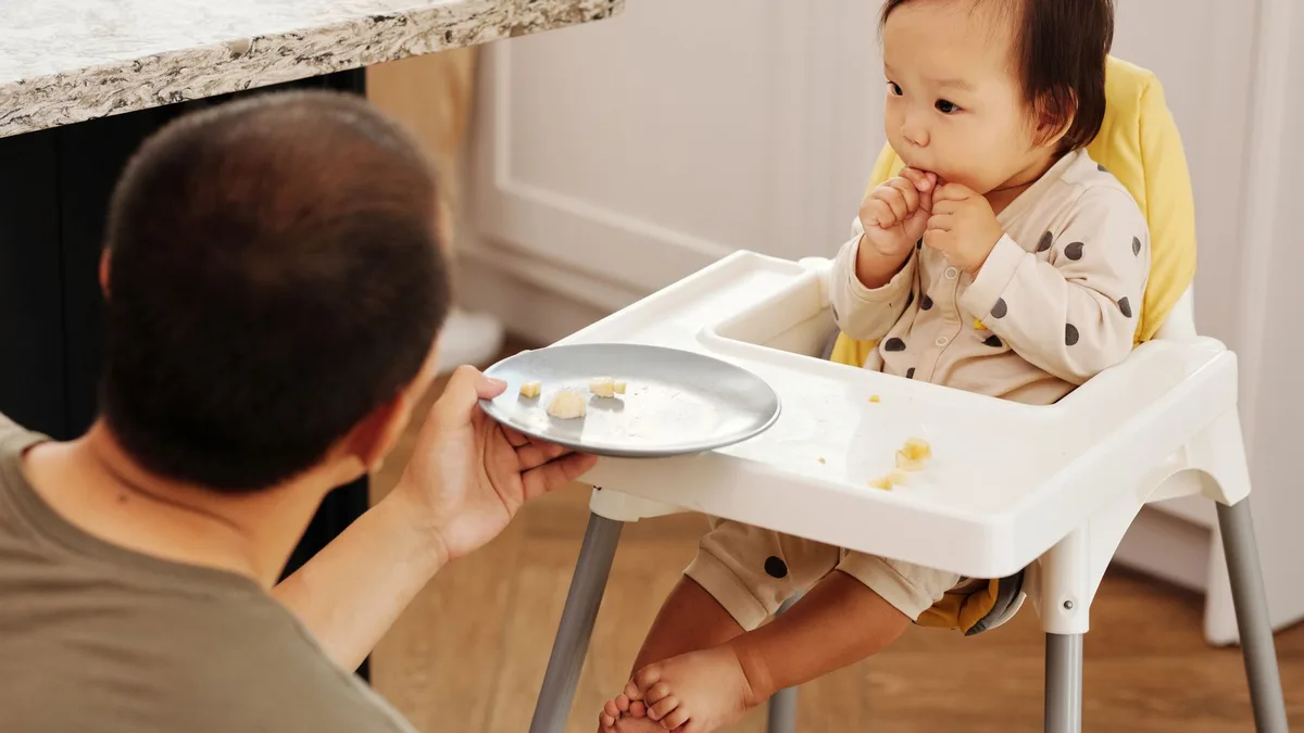 Baby entdeckt gemeinsam mit einem Elternteil feste Nahrung