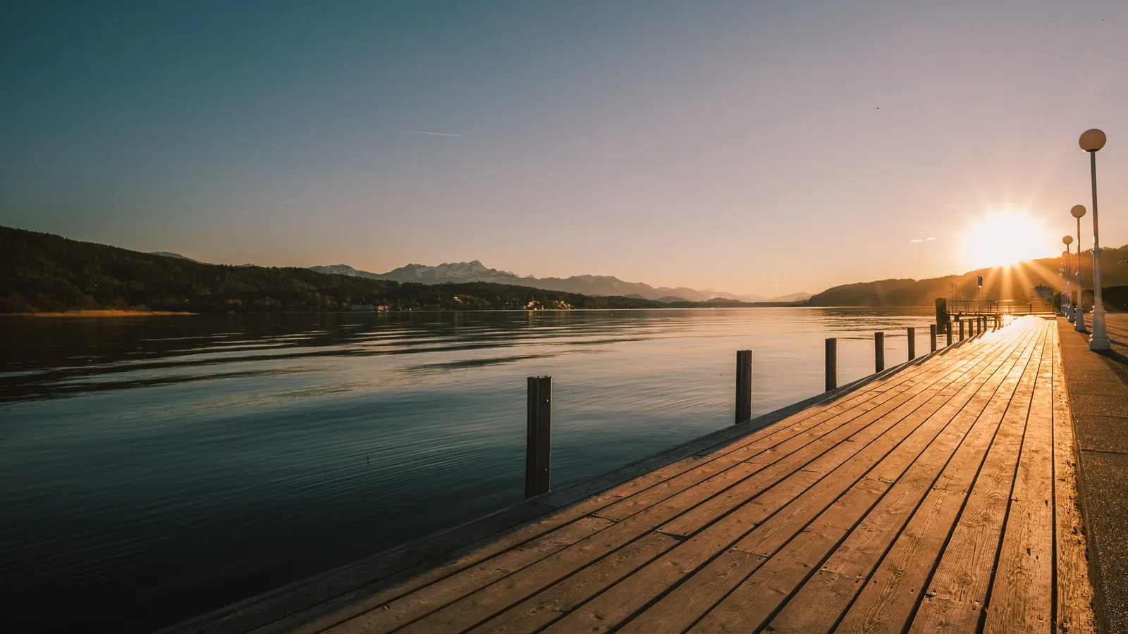 Holzsteg an einem Kärntner See bei Sonnenuntergang, am Horizont Hügel und Berge
