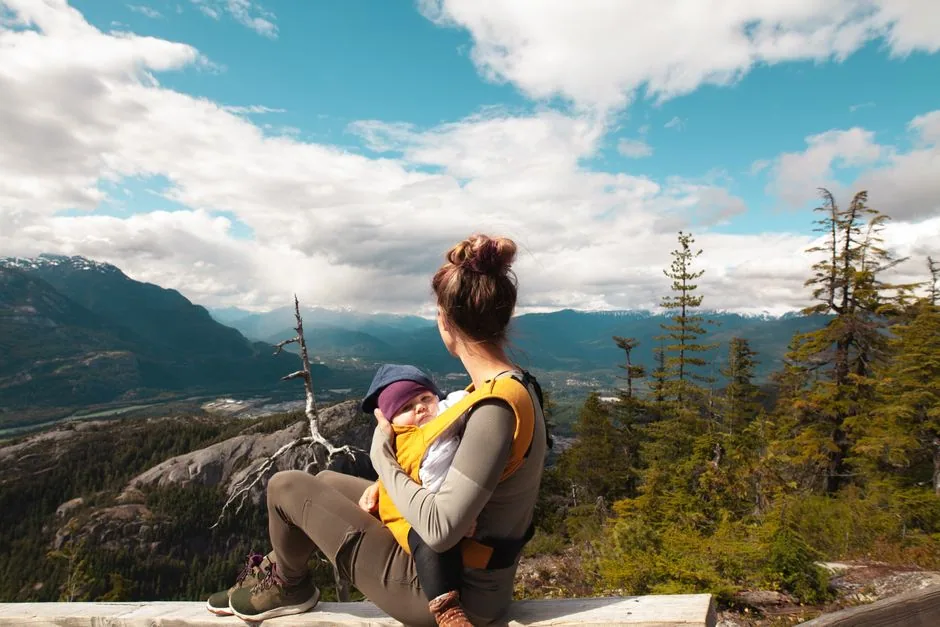 Mutter trägt ihr Baby ergonomisch im Tragetuch mit Blick auf die Berge