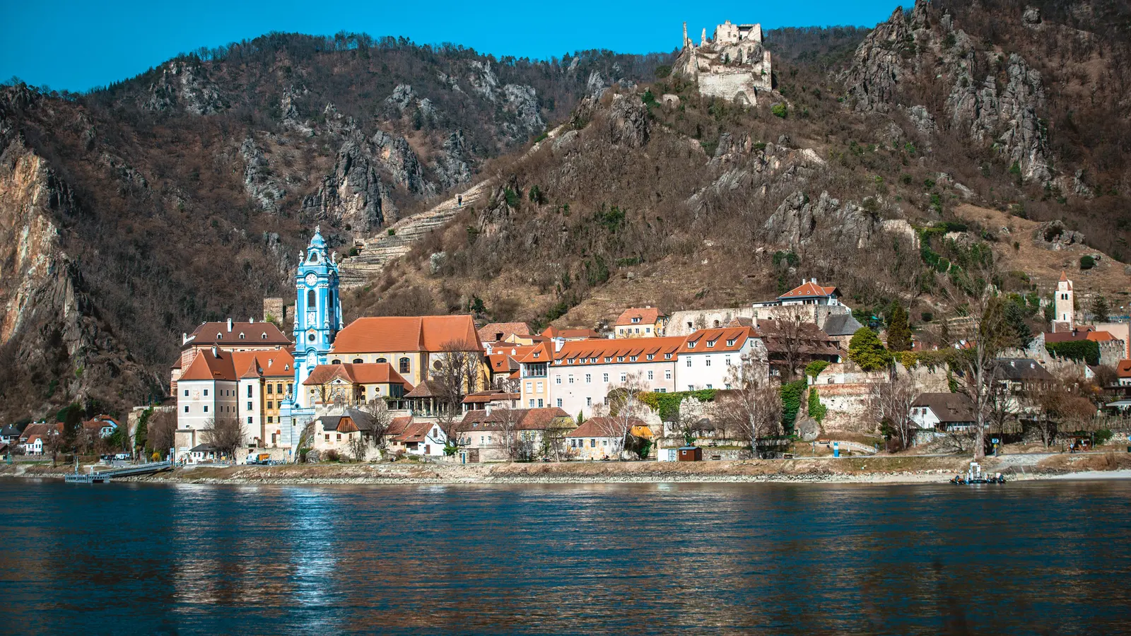 Dürnstein in der Wachau von der Donau aus: der blaue Stiftsturm, darüber die Burgruine auf dem Felsrücken
