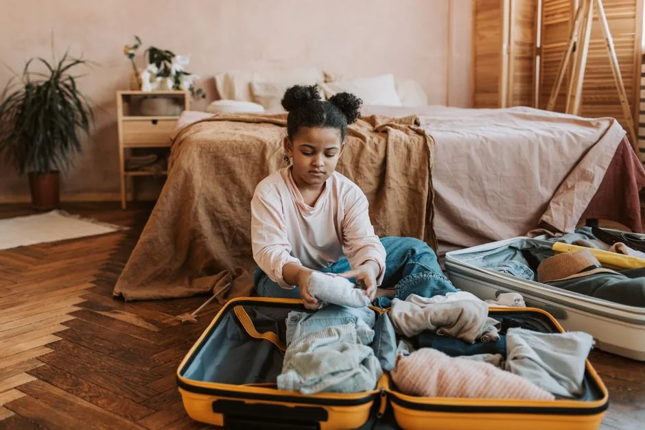 Kind packt aufmerksam Kleidung und Utensilien in einen Reisekoffer