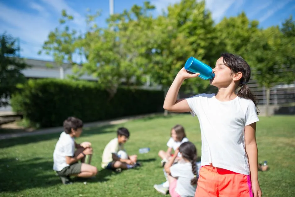 Glückliches Mädchen trinkt erfrischendes Wasser beim Spielen im Freien