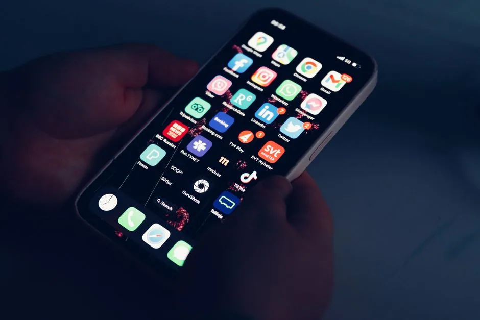 Hände halten ein Smartphone mit bunten App-Icons in abgedunkeltem Raum