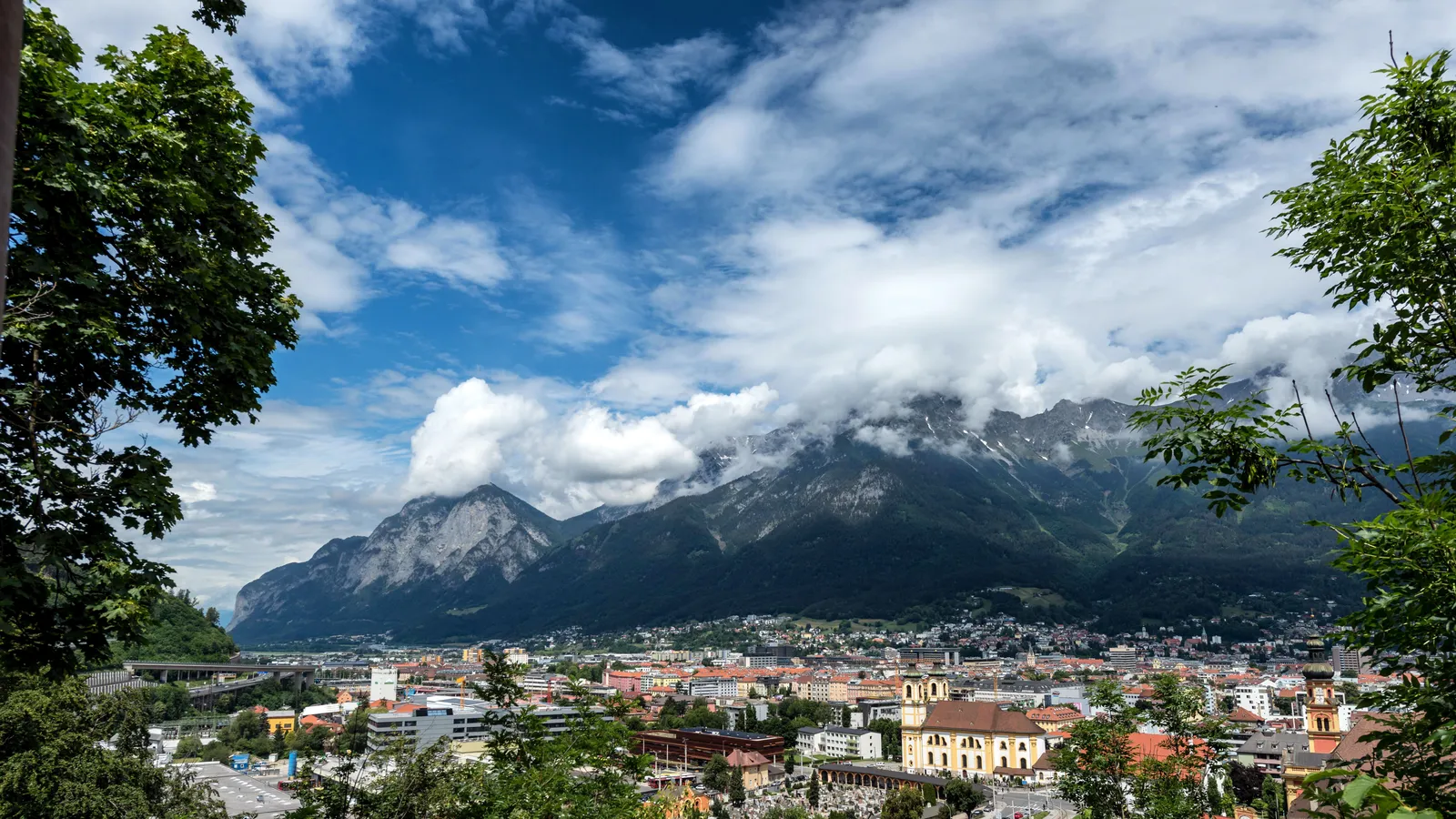 Blick über Innsbruck auf die wolkenverhangene Nordkette, gerahmt von Bäumen